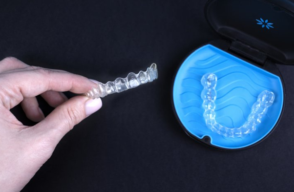 Person holding invisalign aligner whilst another sits in a blue tray